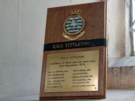 Small brass plaque mounted on wooden stand.
