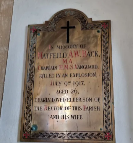 A brass plaque with decorated cross edge and Latin cross dedicated to the subject and detailing the circumstances of his death.