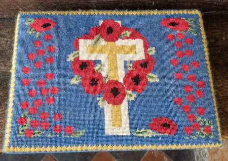 A kneeler with an embroidered image of poppies and a cross and dedication on two of the sides.