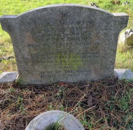 A stone gravestone with an oval top and shoulders and two names in addition to that remembered