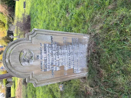 A stone gravestone with a high semi-circle top and curved shoulders with the inscription below joined hands and two names in addition to that remembered.