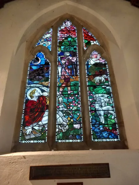 Large stained window featuring allegorical images in west wall of church. Inscribed plaque below