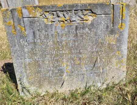 A stone gravestone with a flat top and foliated decoration above the inscription and one name in addition to that remembered