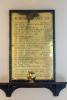 Brass plaque affixed to green marble backboard above wooden shelf. Inscription incised in capital lettering.