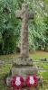 Memorial, constructed of rough-hewn stone, comprises a three-stepped rectangular base surmounted by a tapering shaft with a closed wheel cross. The inscription is on the front face of the middle step.