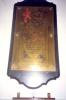 Brass plaque on wooden backboard.