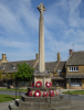 Cross with wreath laid at its base, and houses in the background.