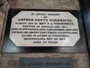 Octagonal Carrara marble tablet on a rectangular black marble backboard. The inscription is engraved in black lettering.
