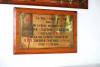 Brass plaque mounted on wood with black and red inscription.