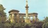 Tall plinth surmounted by column and cross. Behind it is a semi-circular colonnade. Three flights of broad steps lead up to the memorial. Inscription in black lettering on the front face of the plinth.