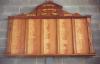 Wall mounted wooden board with triangular pediment, five columns of gold colored inscribed names divided by a raised piece of wood