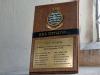 Small brass plaque mounted on wooden stand.