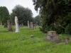 Grave in cemetery, close to tall conifer trees.
