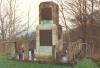 Base surmounted by two staged column. Bronze plaque on the front face of the two stages. Inscription plaque on the lower stage and regimental badge on the upper stage. Whole stands on a paved area with concrete post and chain link fence.