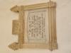 A marble tablet with a cream decorated surround with the impression of an anchor and coiled rope.