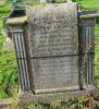 A gravestone with a rolled top and a pillar inserted each side of the inscription with two names in addition to that remembered.