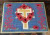 A kneeler with an embroidered image of poppies and a cross and dedication on two of the sides.
