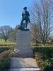 A statue of a soldier stands on a stone base bearing a memorial inscription. Below is a stone plaque with another inscription.