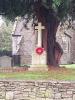 Churchyard view showing stone memorial cross on inscribed plinth and remembrance poppy wreath