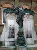 Bronze figure of Victory on cylindrical stone plinth, in front of wall to which plaques are fixed. 