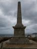 Stone obelisk war memorial on a seafront.