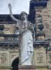 A statue of a woman with her right hand raised and an open book in her left hand.