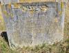 A stone gravestone with a flat top and foliated decoration above the inscription and one name in addition to that remembered