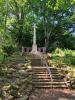 Ryton Urban District WW1/WW2 Cross, with flights of steps leading up to it, and brick wall behind, with WW1 bronze plaques attached.